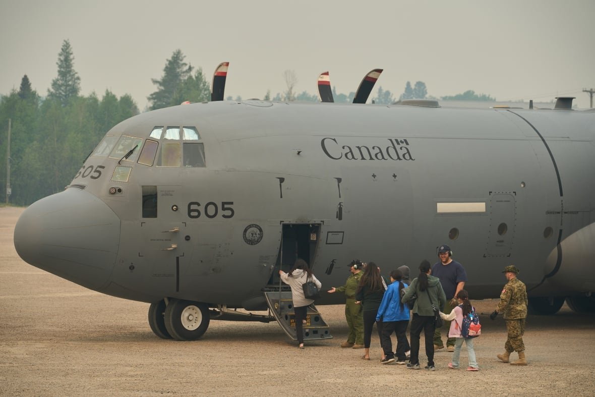 prairies-wildfires-20250603-1 People board a large military aircraft as smoke fills the air around them.