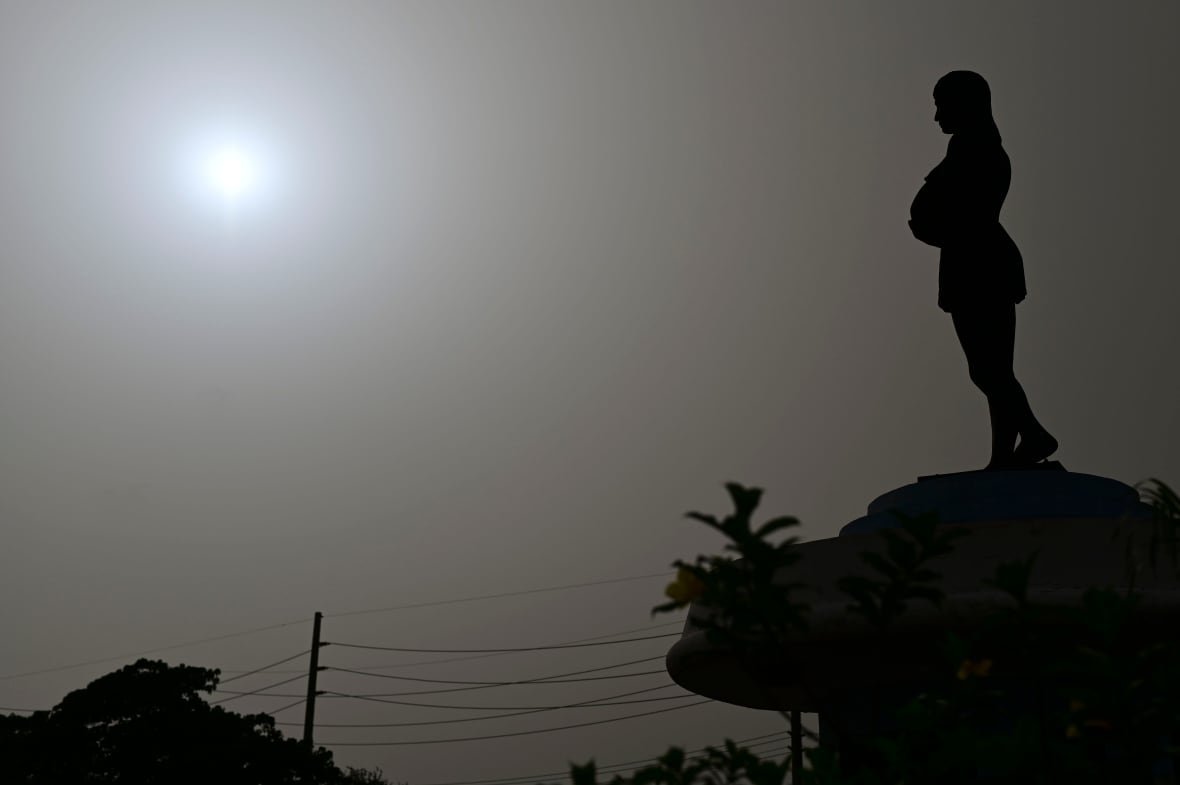puerto-rico-sahara-dust Silhouette of a woman on a hill with the moon or sun in the sky blurred by dust