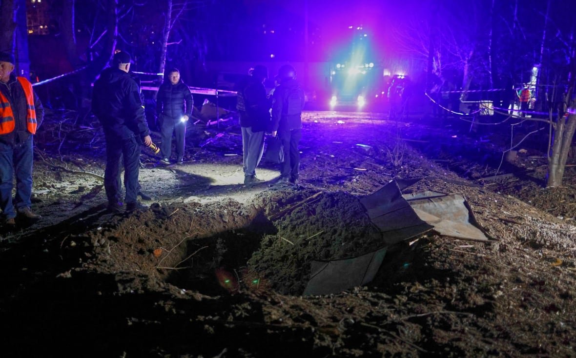 russia-ukraine-war Emergency responders stand near a crater in a road.