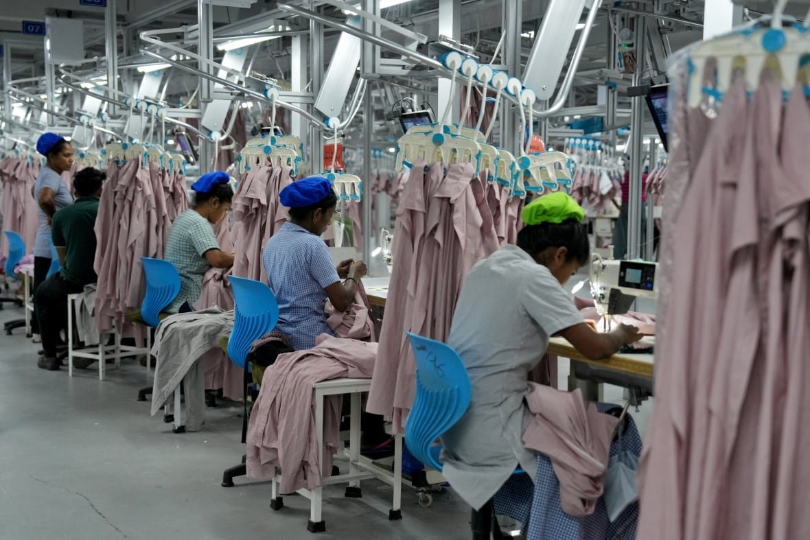 usa-trump-tariffs-sri-lanka-1 A garment factory is shown, with four or five women with their backs to the camera sitting and working at tables.