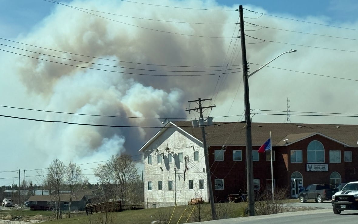 wildfires-near-pimicikamak-cree-nation-may-2025-3 A plume of smoke billows from behind a building in Pimicikamak Cree Nation.