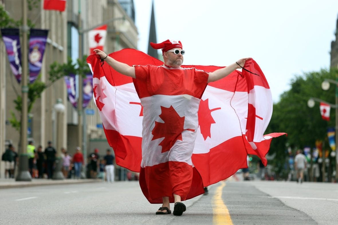A person draped in a Canadian flag walks down a street.