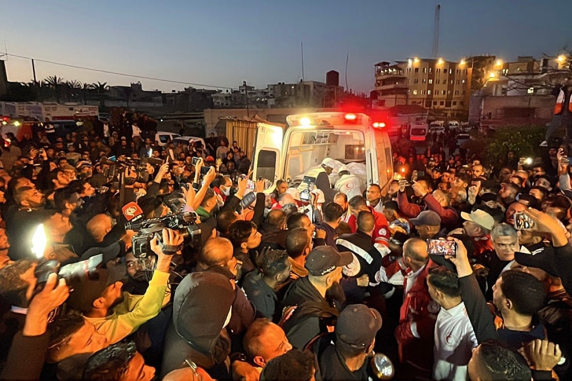Several people, many with cameras, crowd around an ambulance.