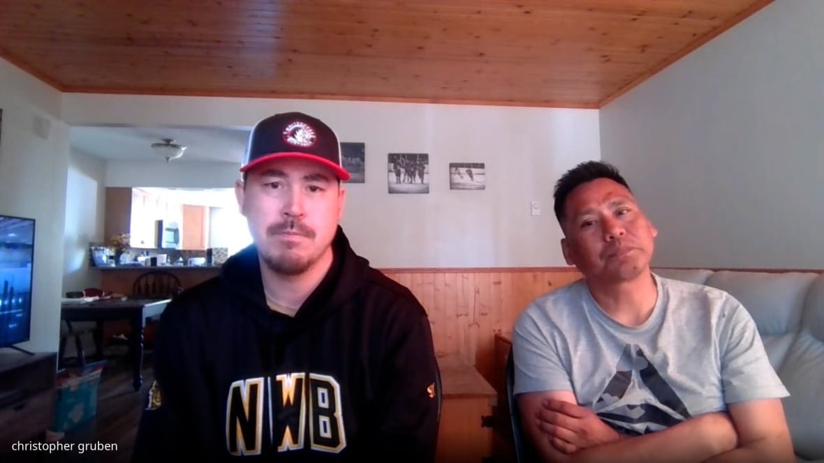 Two men in a room stare straight.