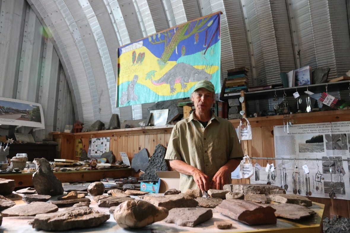 A man stands behind a large collection of rocks and fossils.
