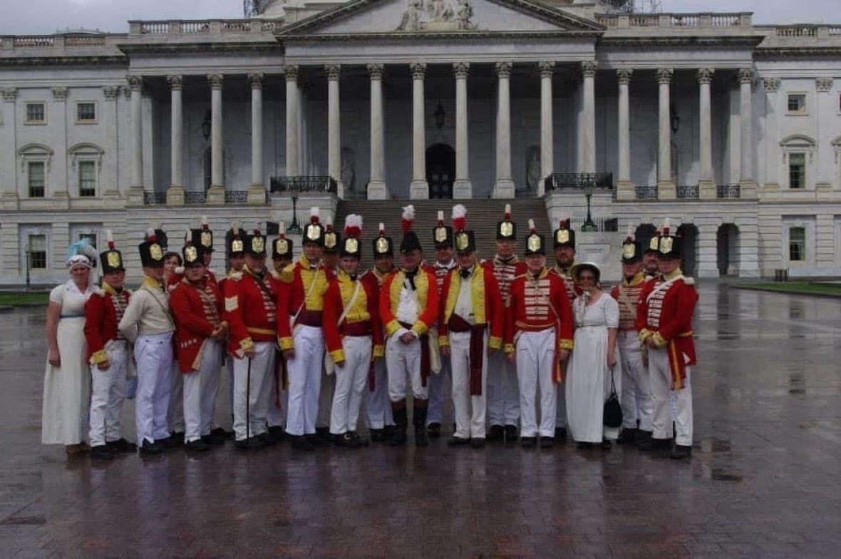 People in old soldier uniforms stand in front of a building.