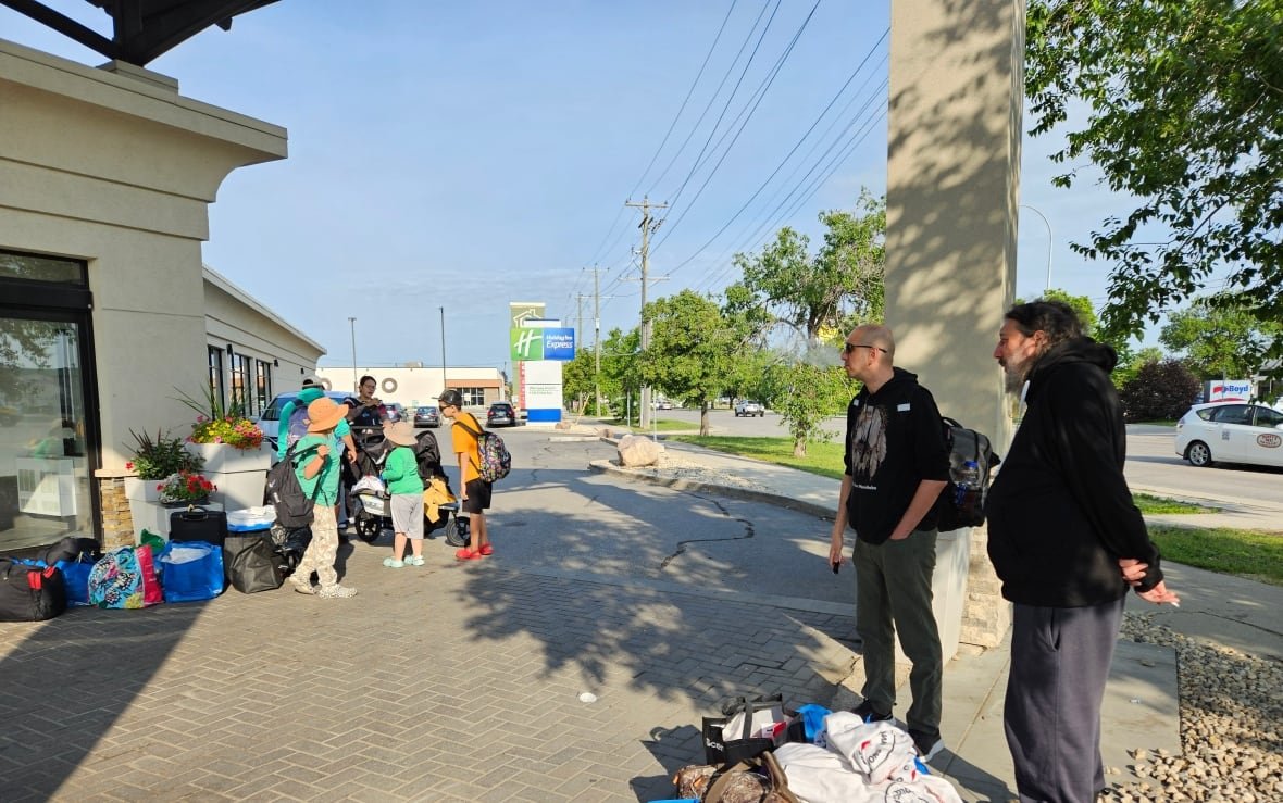 flin-flon-evacuees-at-winnipeg-holiday-inn-prepare-to-return-home A group of people stand outside a hotel with their bags.