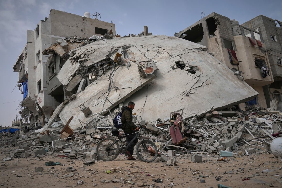 A man with a bicycle walks past a badly damaged building.