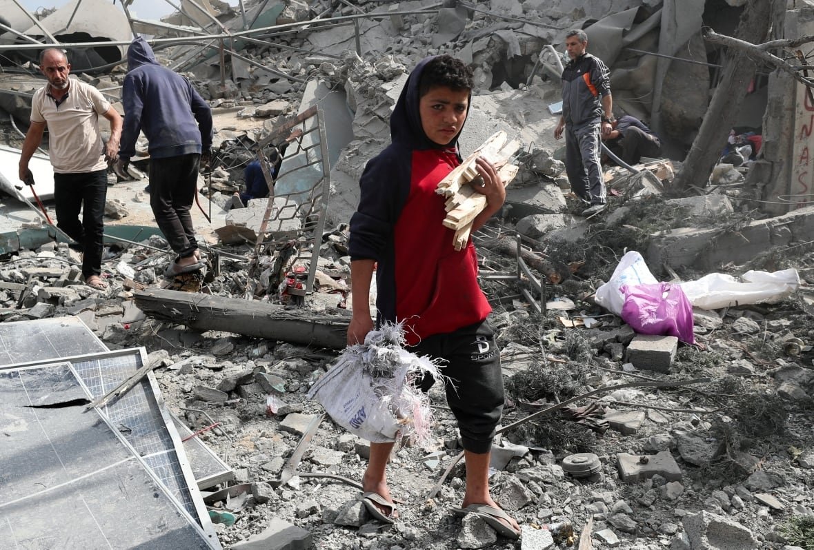 A boy walks on top of rubble with wood in hand.