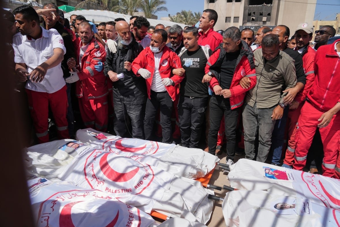 israel-palestinians Mourners gather around body bags during an outdoor funeral.