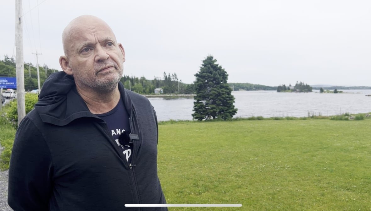 A bald man wearing a hoodie is shown, with a body of water in the background.
