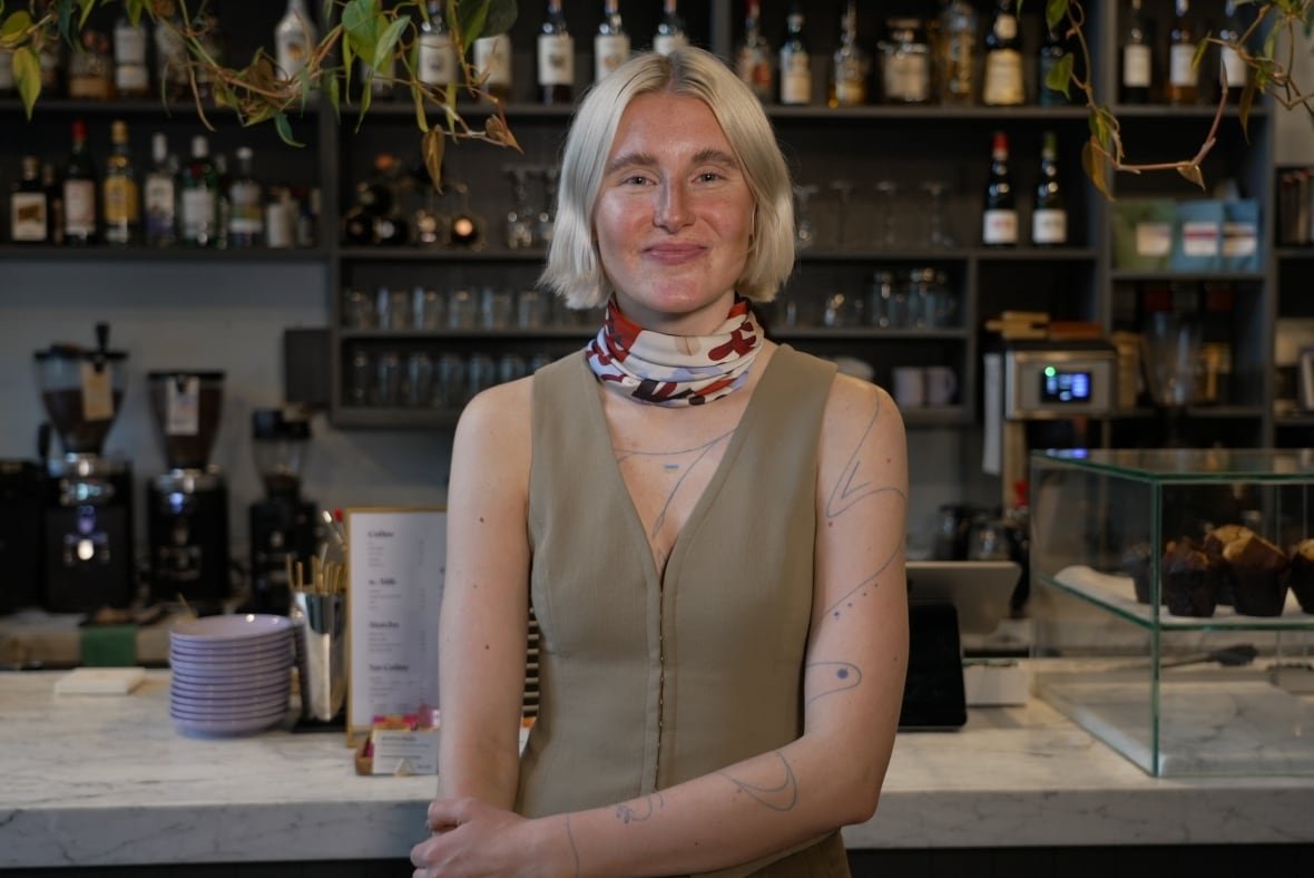 nadiia-semenichenko A woman stands in front of a barista counter in a cafe.