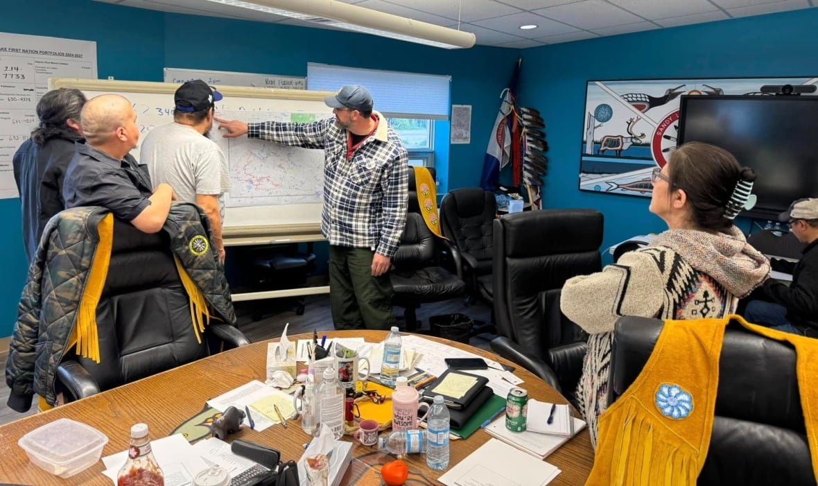 sandy-lake-first-nation-leadership People are seen standing in a room, pointing at a chart.