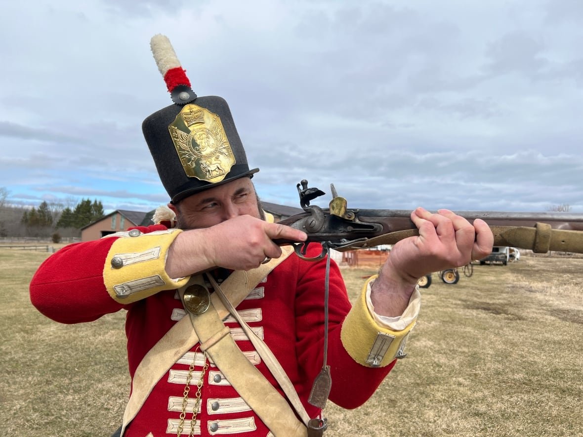 A man in an old military uniform shoots a rifle.
