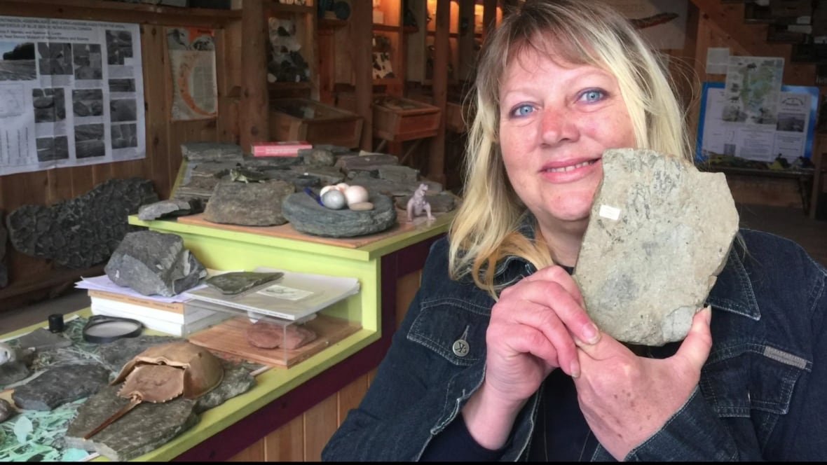 A woman smiles and holds up a fossil.
