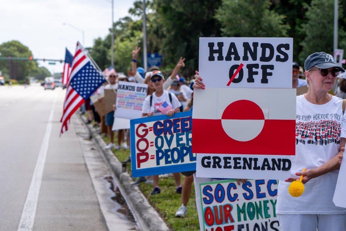 trump-protests Protesters hold up signs on the side of a road.