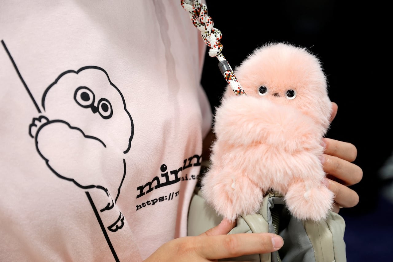 A person carrying a pink stuffed robot on a leather bag.
