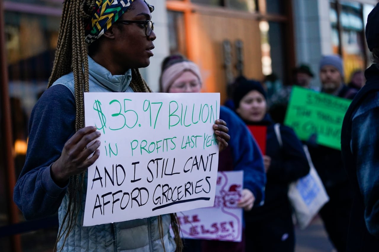 A person holds up a sign that says, "$35.97 billion in profits last year and I still can't afford groceries"