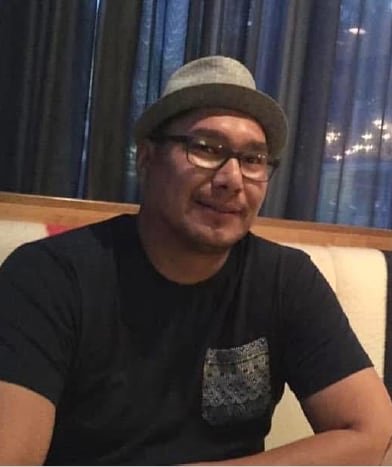 A young Indigenous man wearing a hat and t-shirt smiles