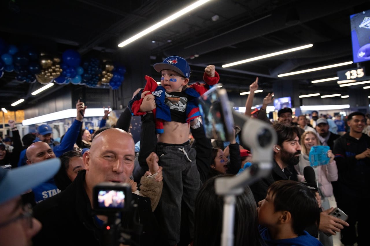 A man holding a toddler dressed in Toronto Blue Jays attire in a celebratory arena setting.
