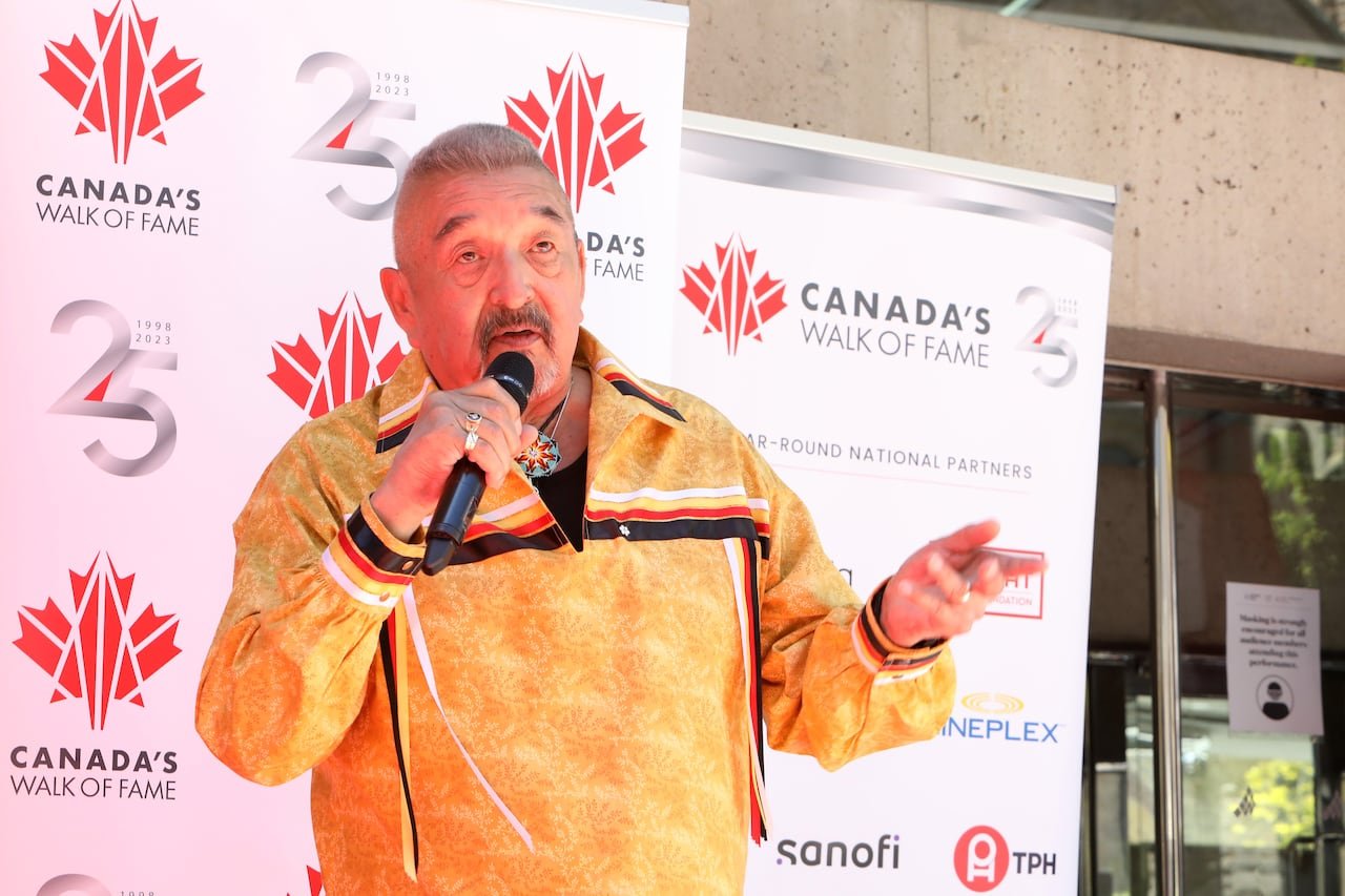 default-135 A man with short cropped grey hair and a mustache is shown speaking into a microphone while speaking at an outdoor event.