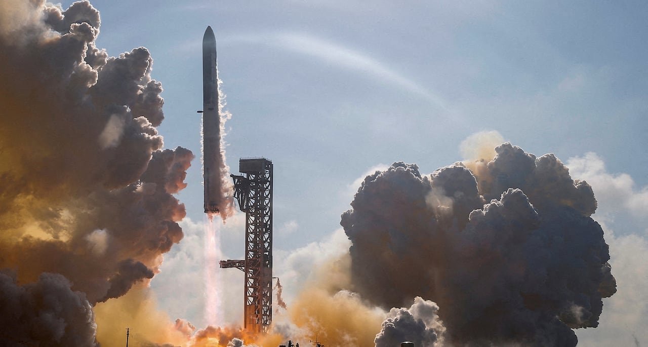 A large rockets blasts into the air with clouds forming around it.