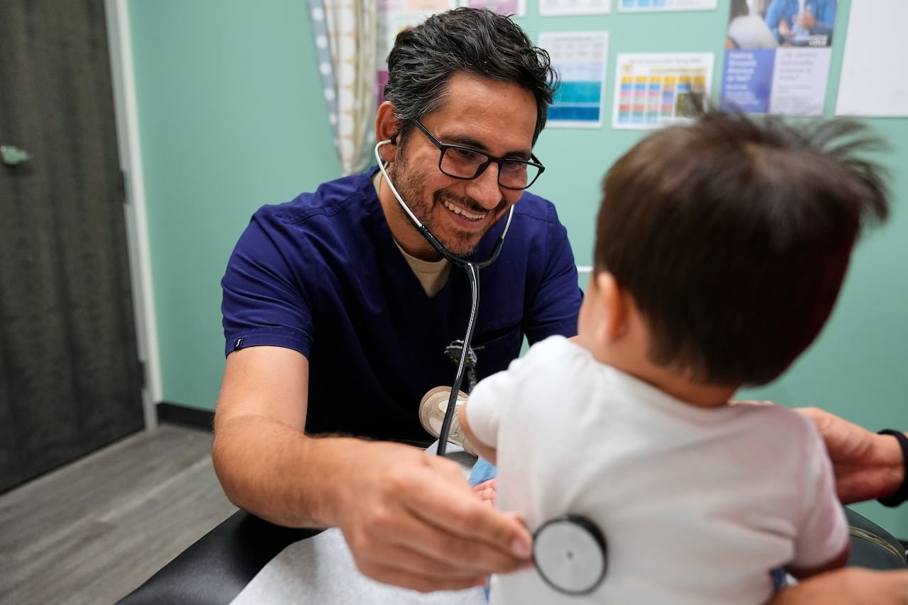 default-176 A pediatrician smiles as he listens through a stethoscope held against the back of a 16-month-old boy.