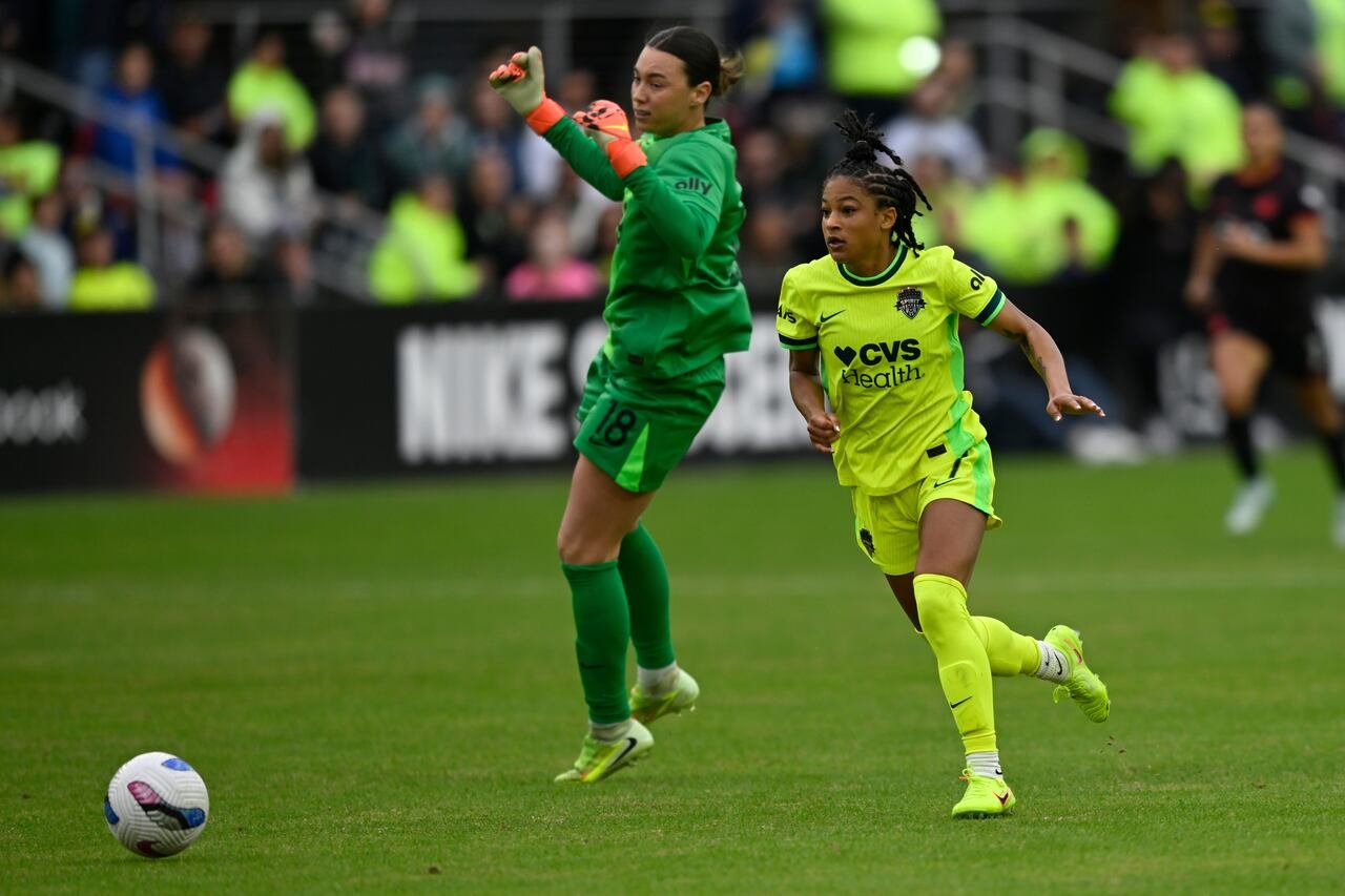default-16 A female soccer player in a bright yellow and green uniform gets past an opposing goalkeeper.